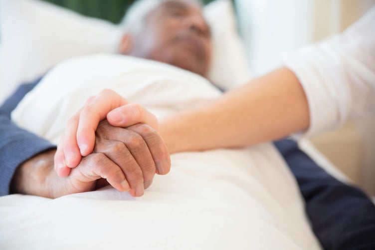 Young person holding hand of sleeping or dying patient in hospital bed