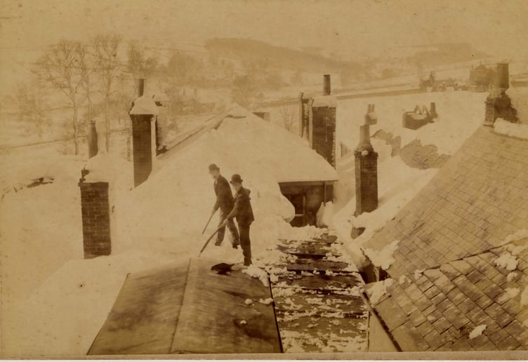 March 1891. Two men clearing snow from a roof on the west side of Fore Street, Kingsbridge, after the blizzard. Possibly the workhouse on the far right.