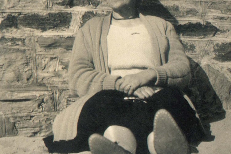 An unknown lady sitting in front of a wall on the beach possibly at Salcombe